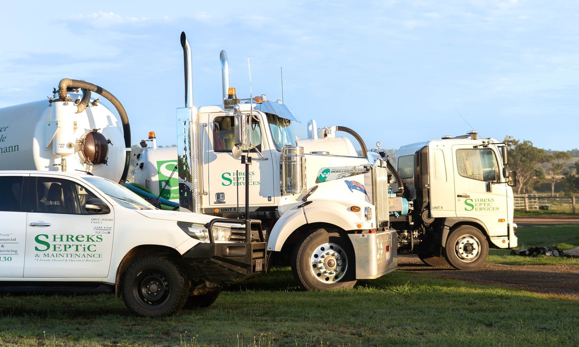 Three White Utility Trucks Parked on Grass — Shreks Septic Services in Gowrie Junction, QLD