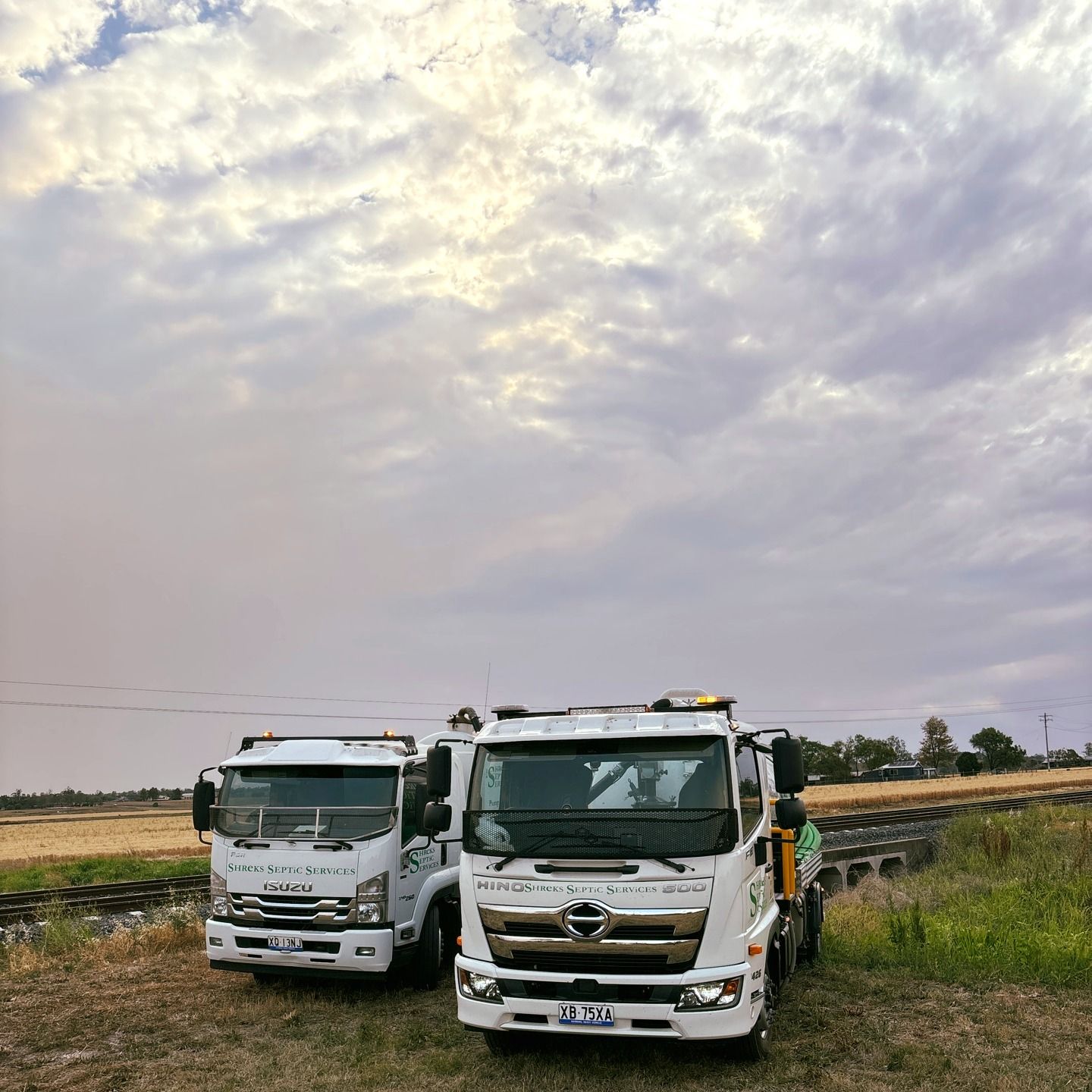 Two White Trucks Parked Side by Side in a Grassy Field — Shreks Septic Services in Hampton, QLD