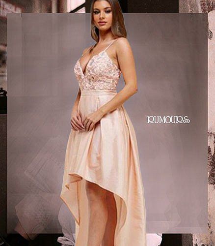Woman in peach-colored formal dress, high-low hemline, posing indoors.