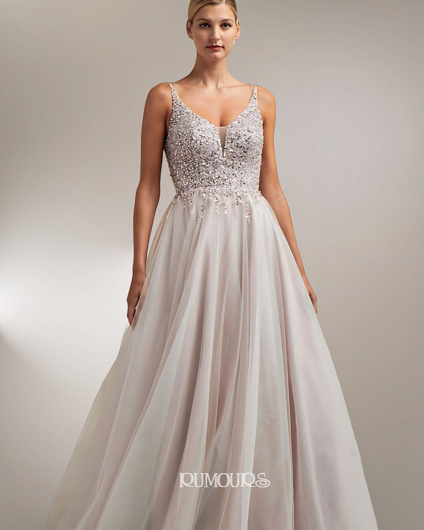 Woman in a light-colored formal gown with embellished bodice, spaghetti straps, and flowing skirt, posing indoors.