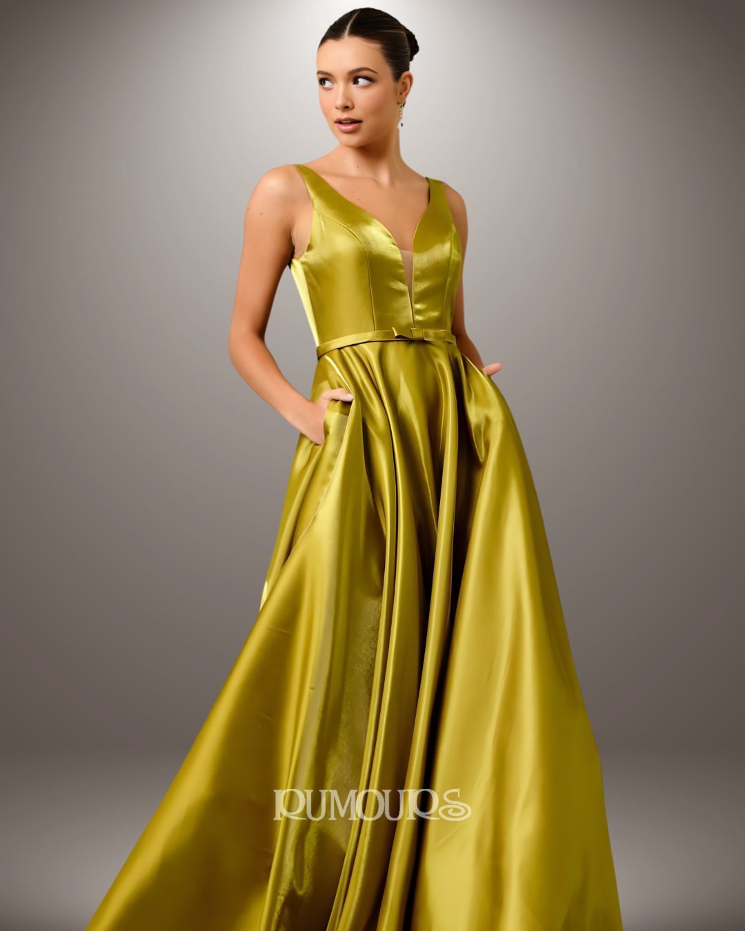 Woman in a gold satin gown with pockets, standing against a neutral gray background.