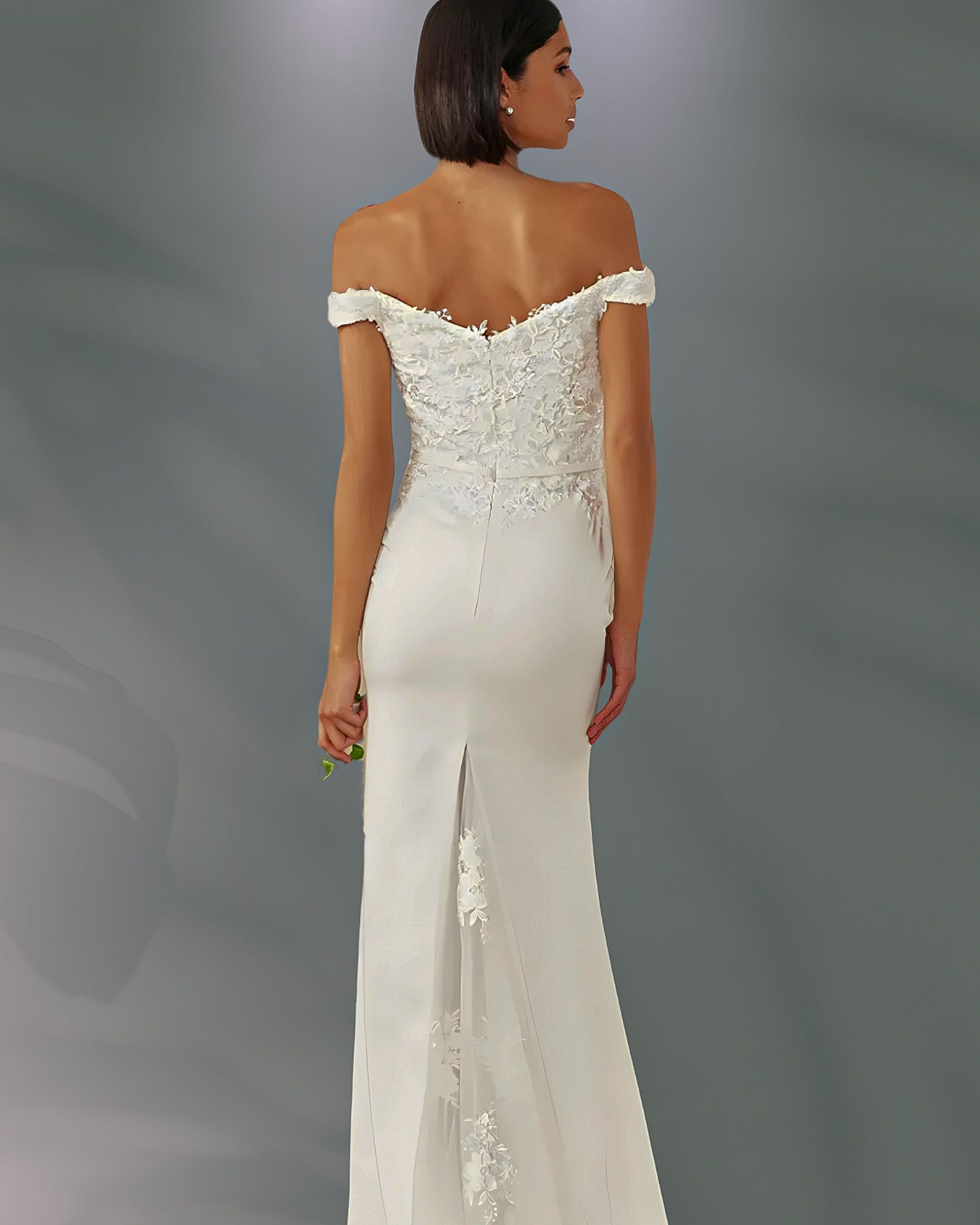 Woman in off-the-shoulder white wedding dress, back view, standing in front of a gray backdrop.