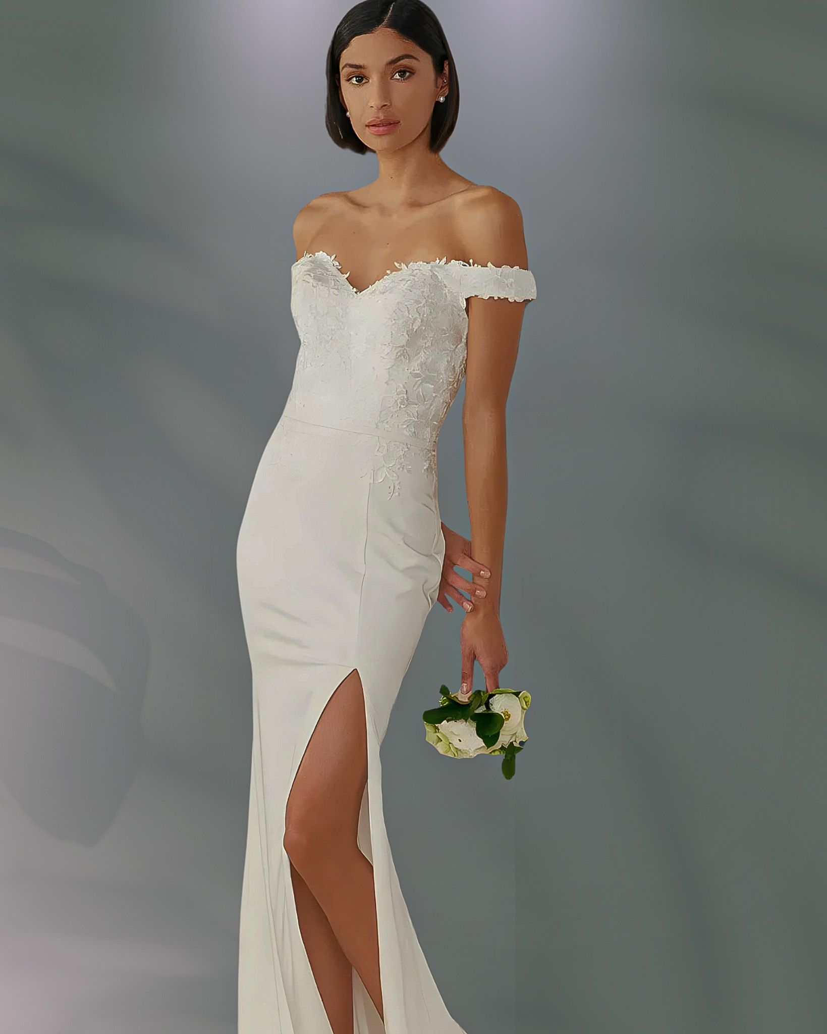 Woman in an off-the-shoulder white wedding dress with a high slit, holding a small bouquet.