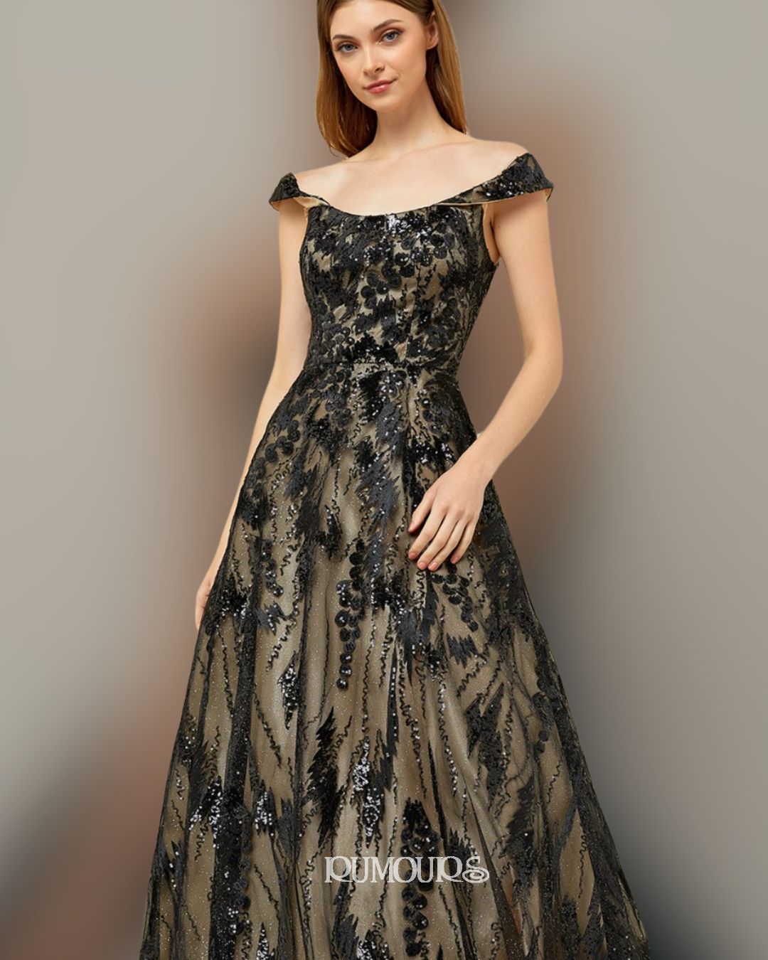 Woman in a black and gold off-the-shoulder gown, posing in front of a neutral background.