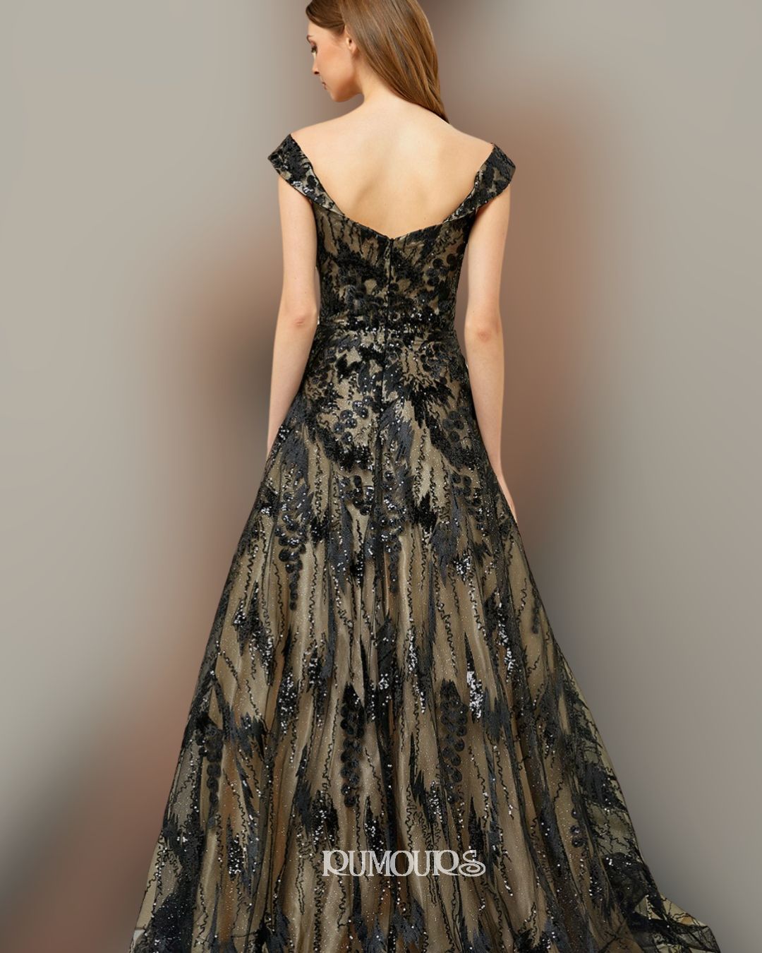 Woman in a black and tan embellished formal gown, standing against a neutral background.