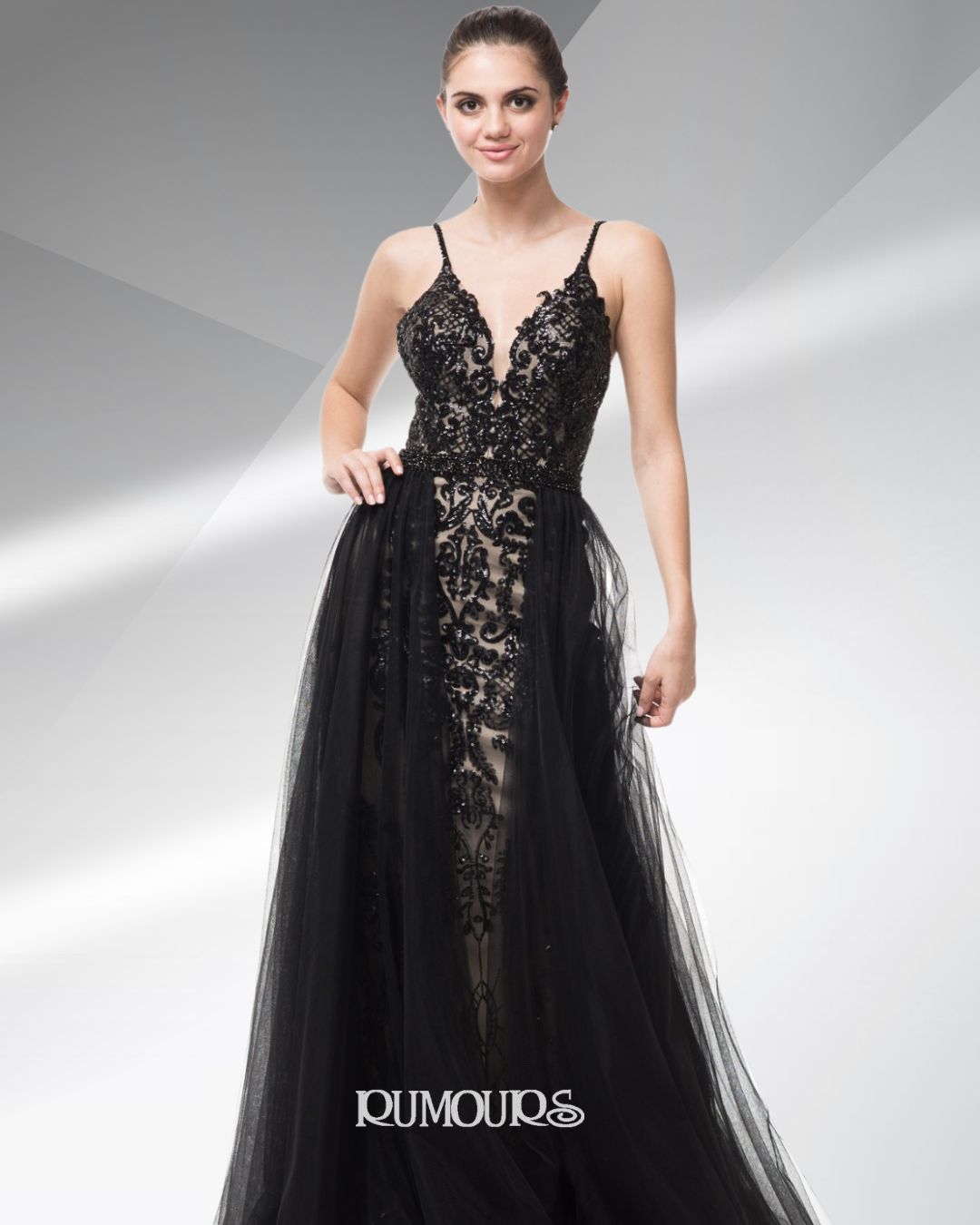 Woman in a black evening gown with spaghetti straps and a flowing skirt, standing in a studio.
