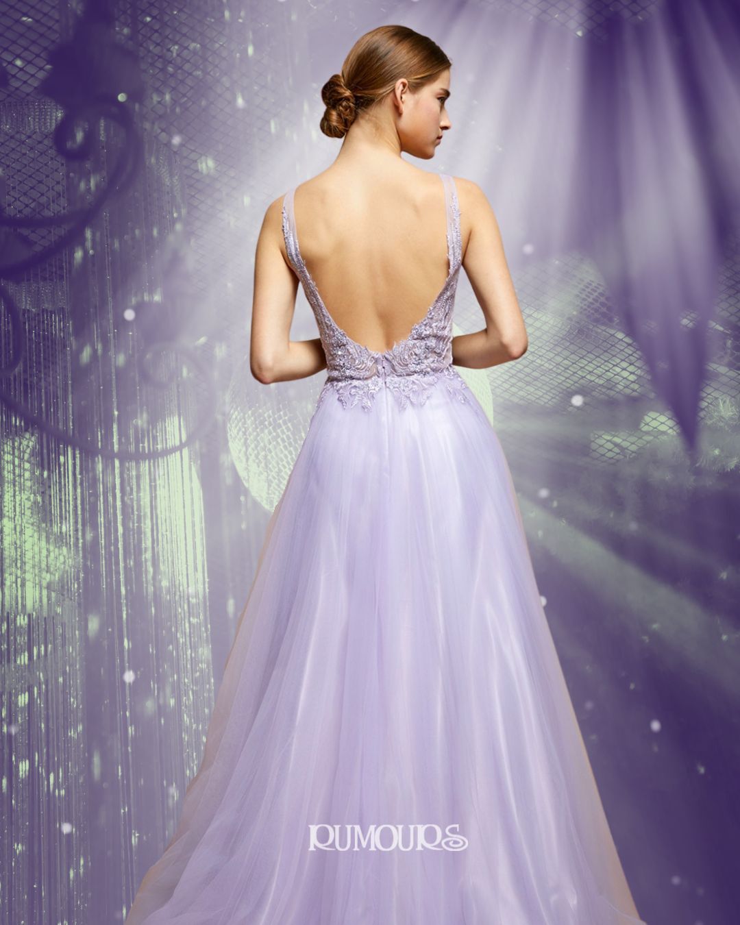 Woman in a lavender gown with open back, standing, facing away. Backlit, with purple, ethereal background.