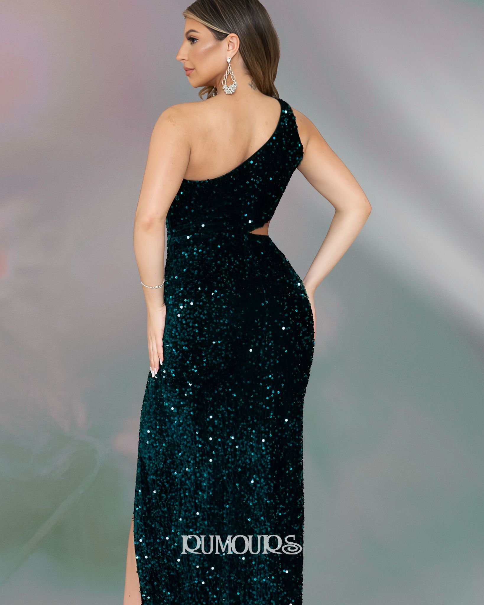 Woman in dark green, sequined, one-shoulder gown, side pose, hand on hip.