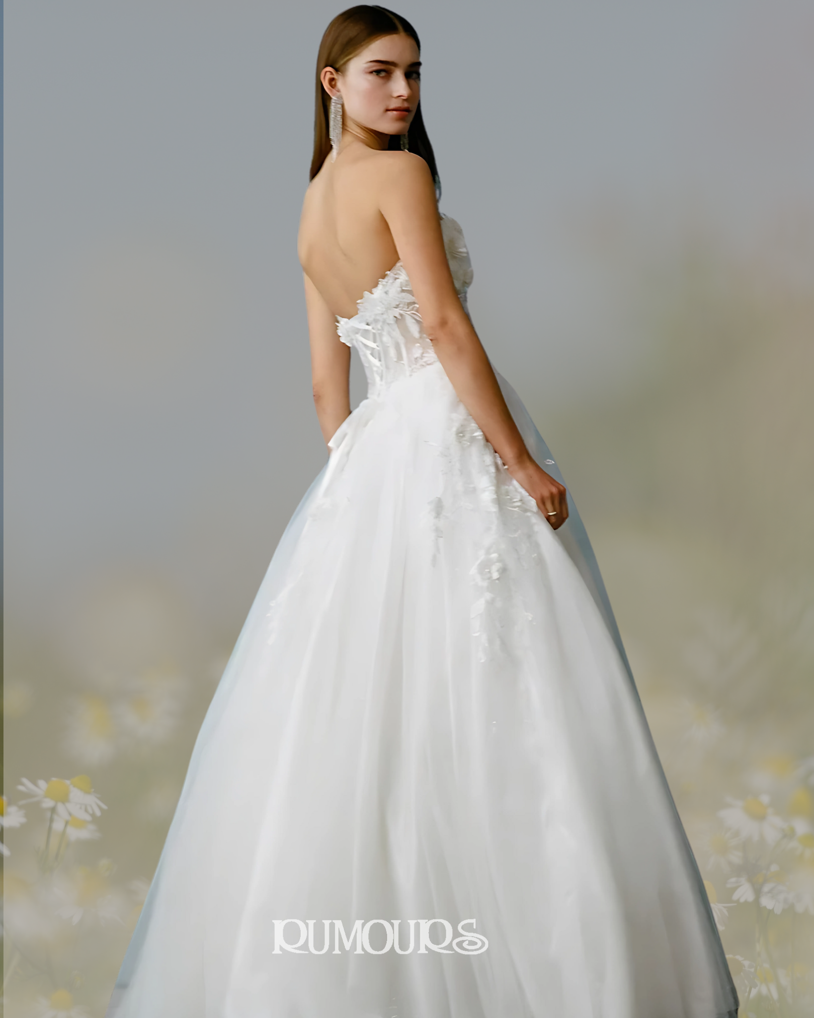 Woman in strapless white wedding dress, facing slightly away. Embroidered floral details, outdoor setting.