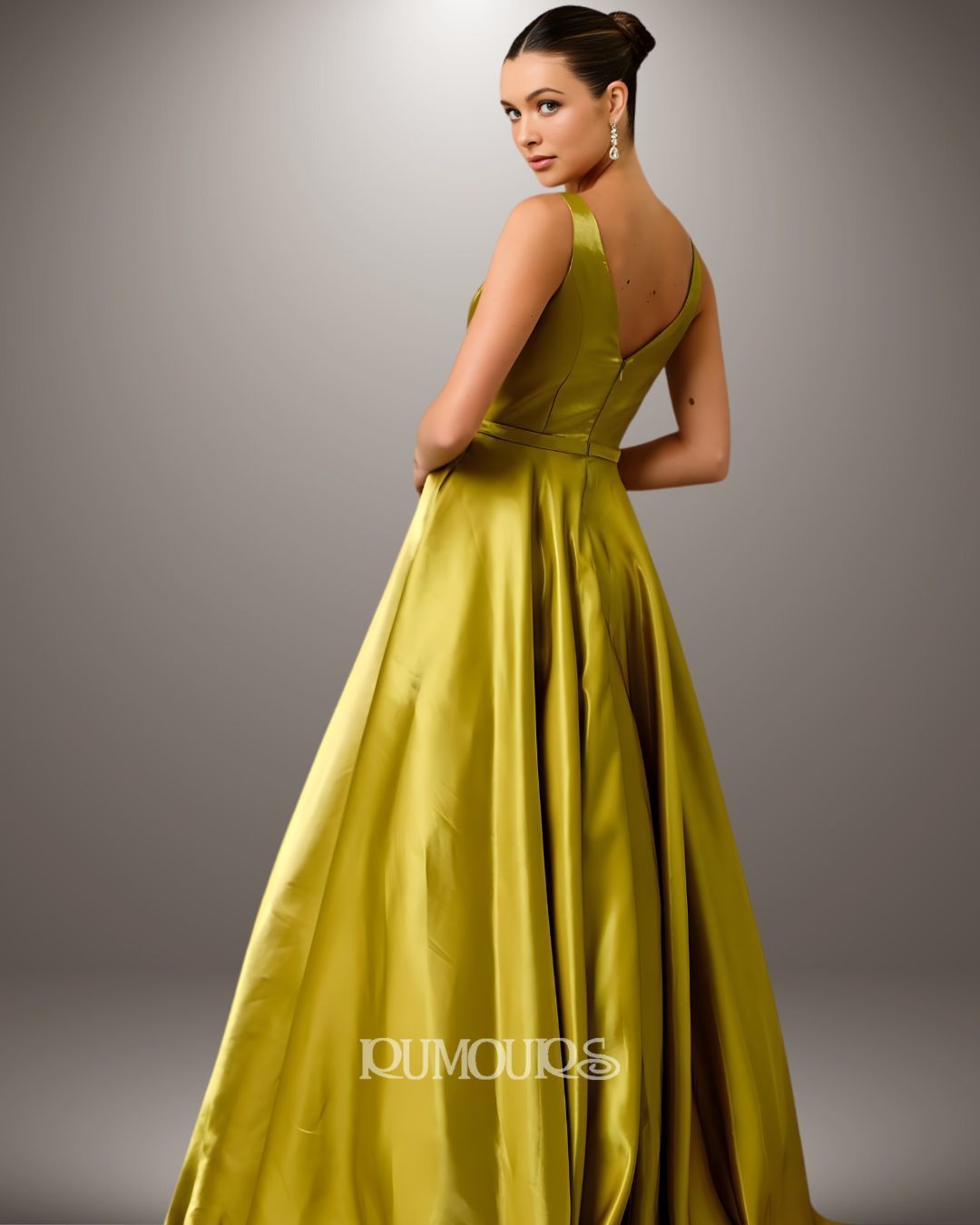 Woman in a long, olive-green evening gown, looking over shoulder, posed in studio setting.