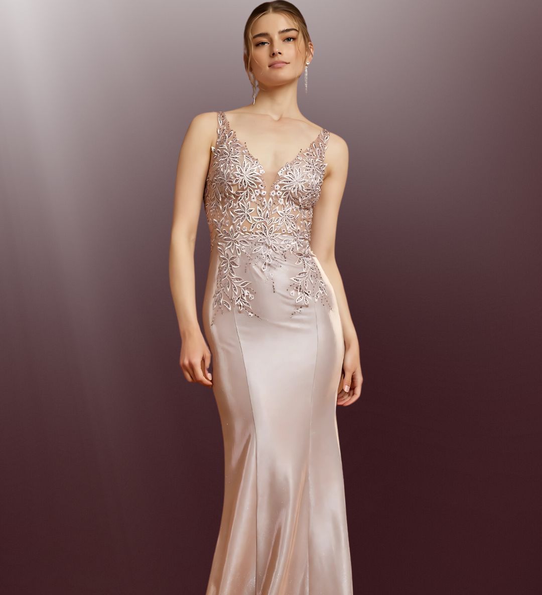 Woman in formal, champagne-colored gown with jeweled bodice, standing in a studio with a dark red background.
