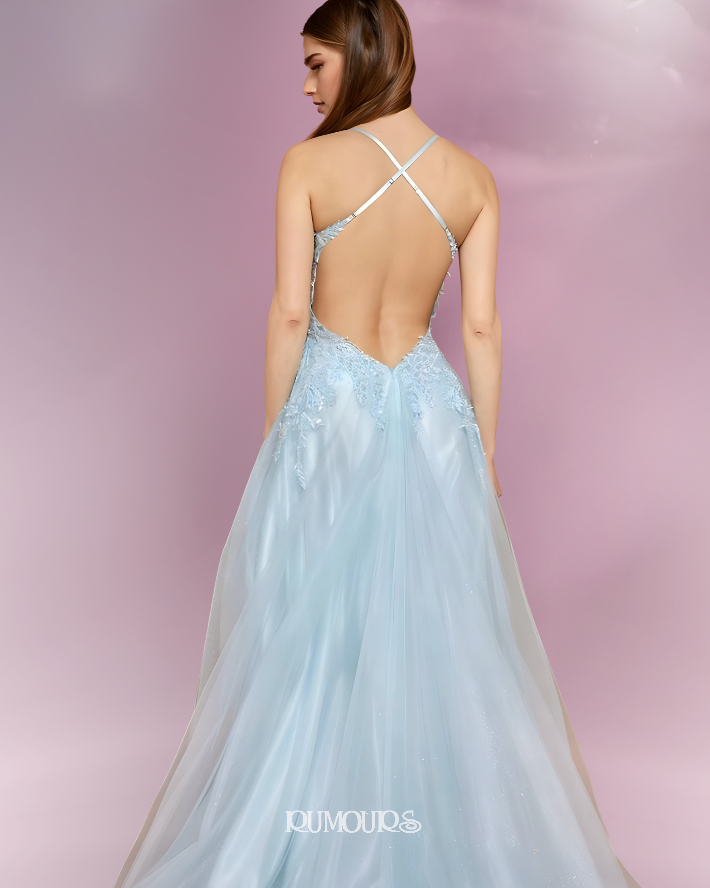 Woman in a light blue formal gown with an open back, standing against a pink backdrop.