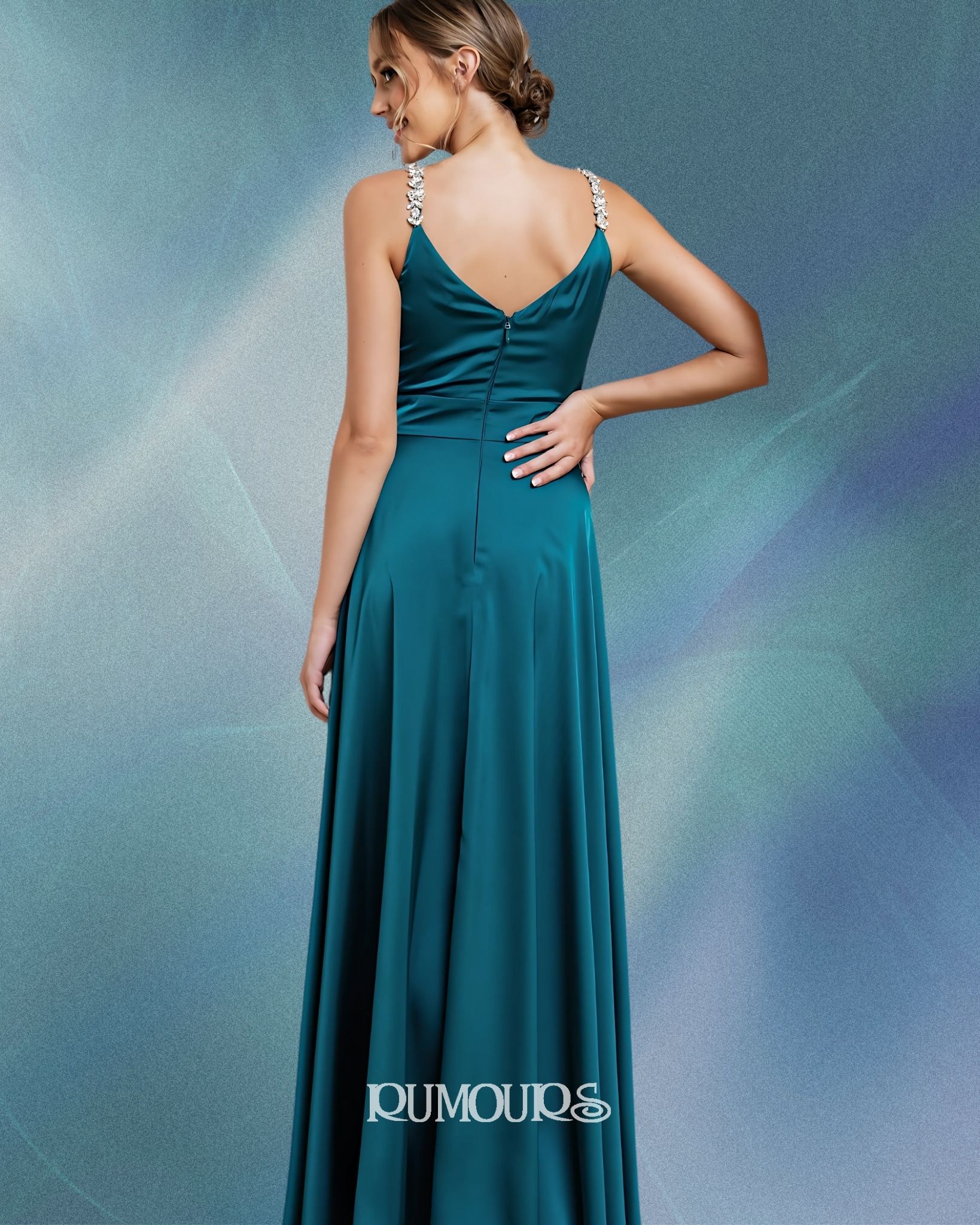 Woman in teal evening gown with jeweled straps, standing with hand on hip.