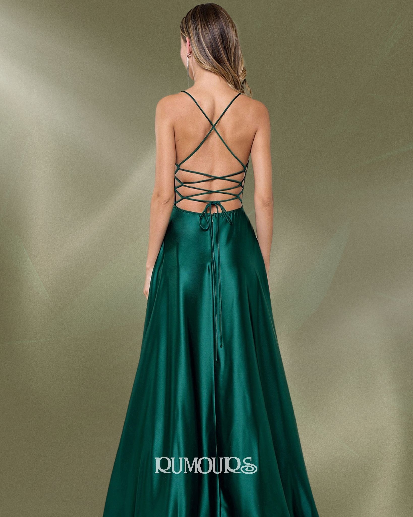 Woman in a green satin gown with crisscross back, standing in front of a textured background.