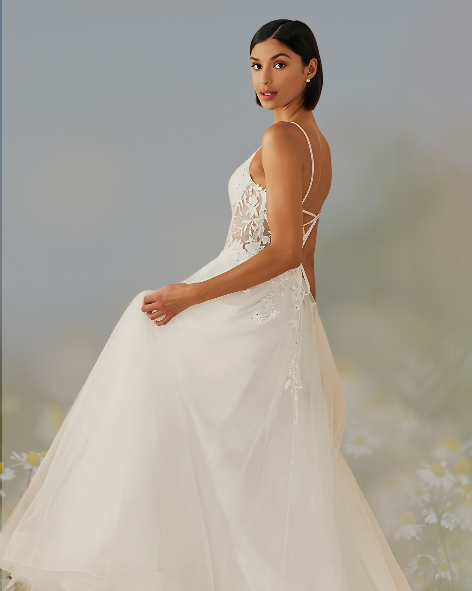 Woman in white wedding dress, turned, looking over shoulder. Dress has sheer bodice, open back, full skirt, and spaghetti straps.