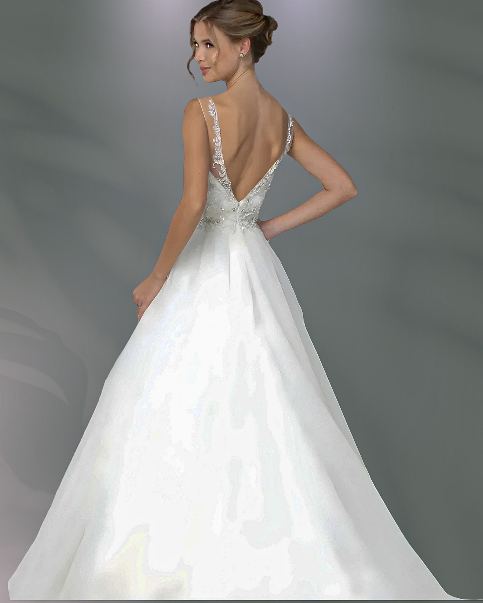 Woman in white wedding dress, back view; low back, delicate straps, light tulle skirt, standing.