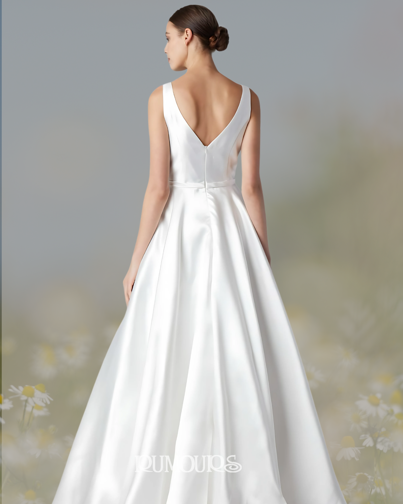 Woman in white wedding dress, back view, deep V-neck, floor-length skirt, bun hairstyle, outdoor setting.