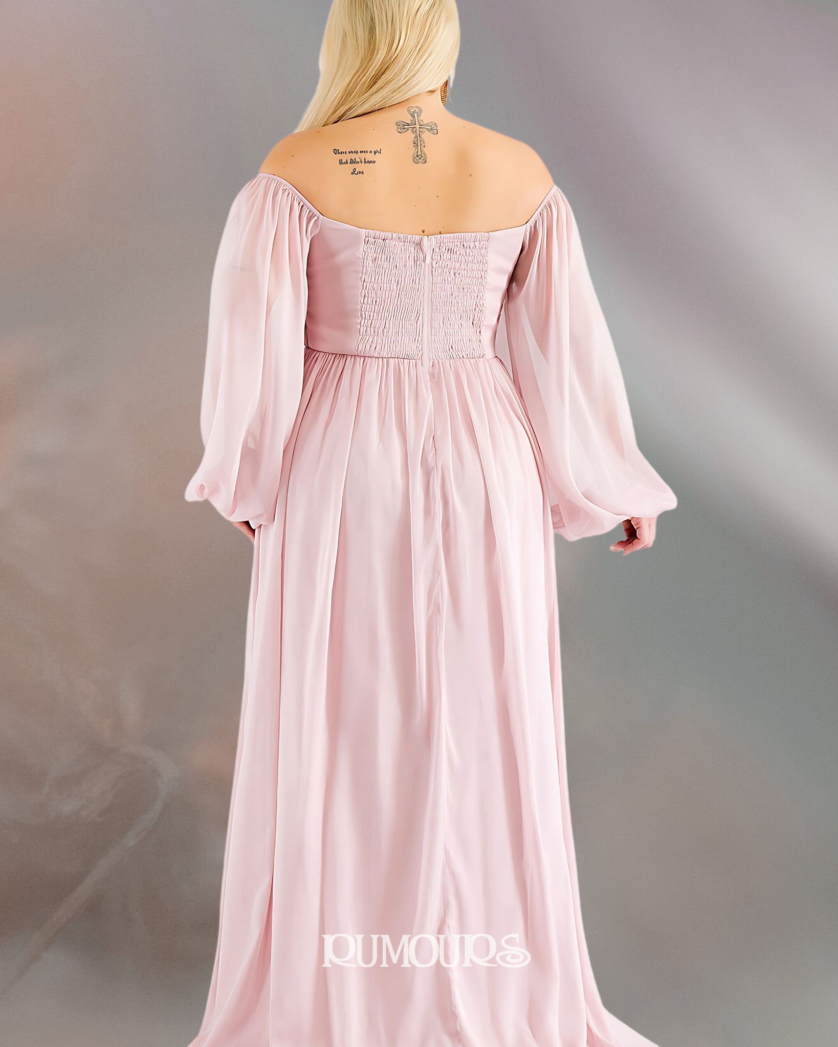 Woman wearing a long, pink off-the-shoulder gown with long sleeves. The dress has a lace back and flowing skirt.