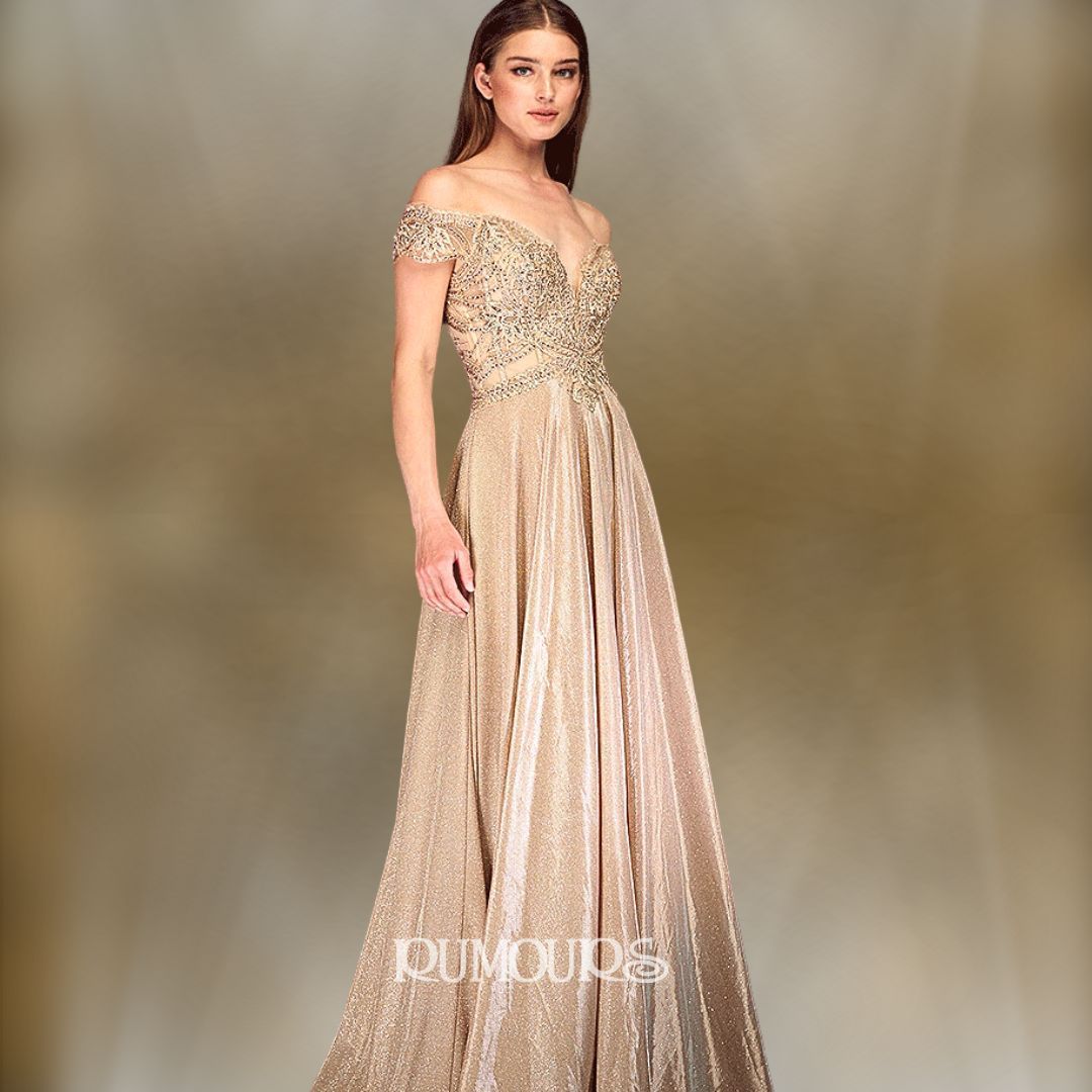 Woman in a gold off-the-shoulder gown, posing in a studio with a neutral background.