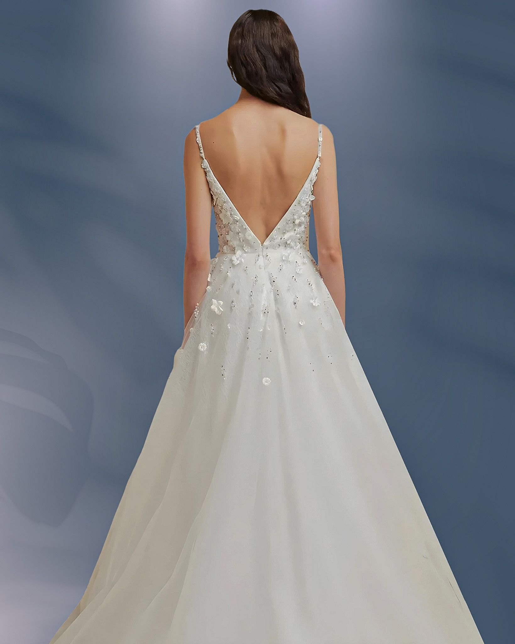 Back view of a woman wearing a white wedding gown with a low back, embellished with sequins and floral appliqués.