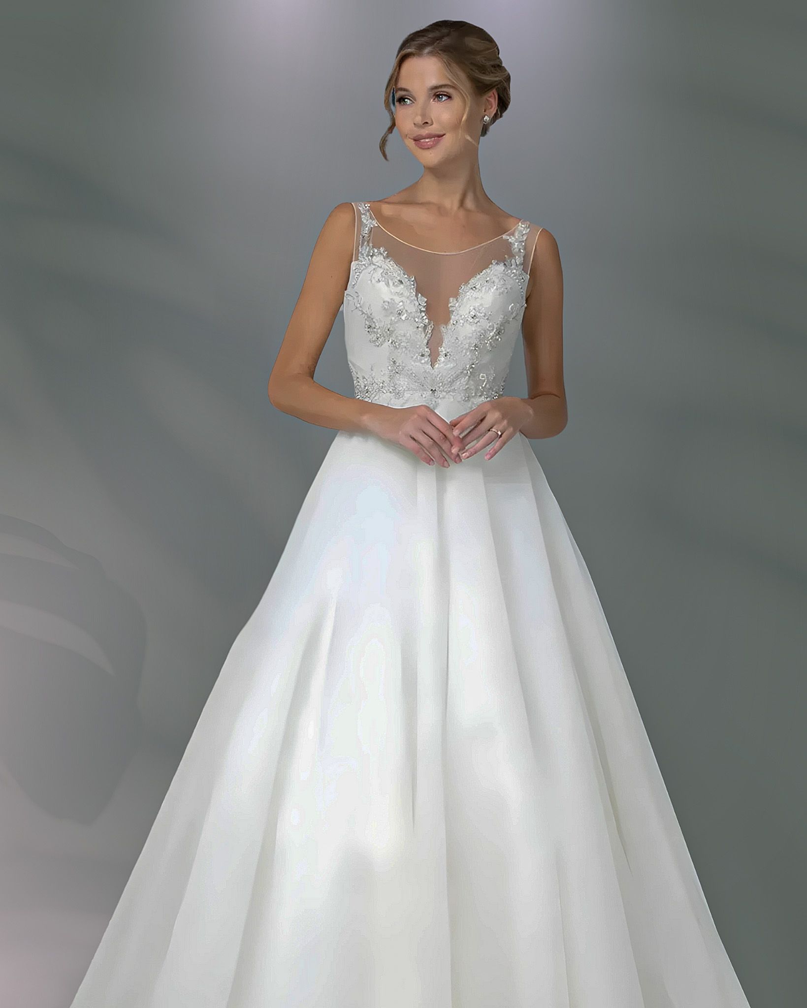 Woman in white wedding dress with sheer neckline, posing indoors.
