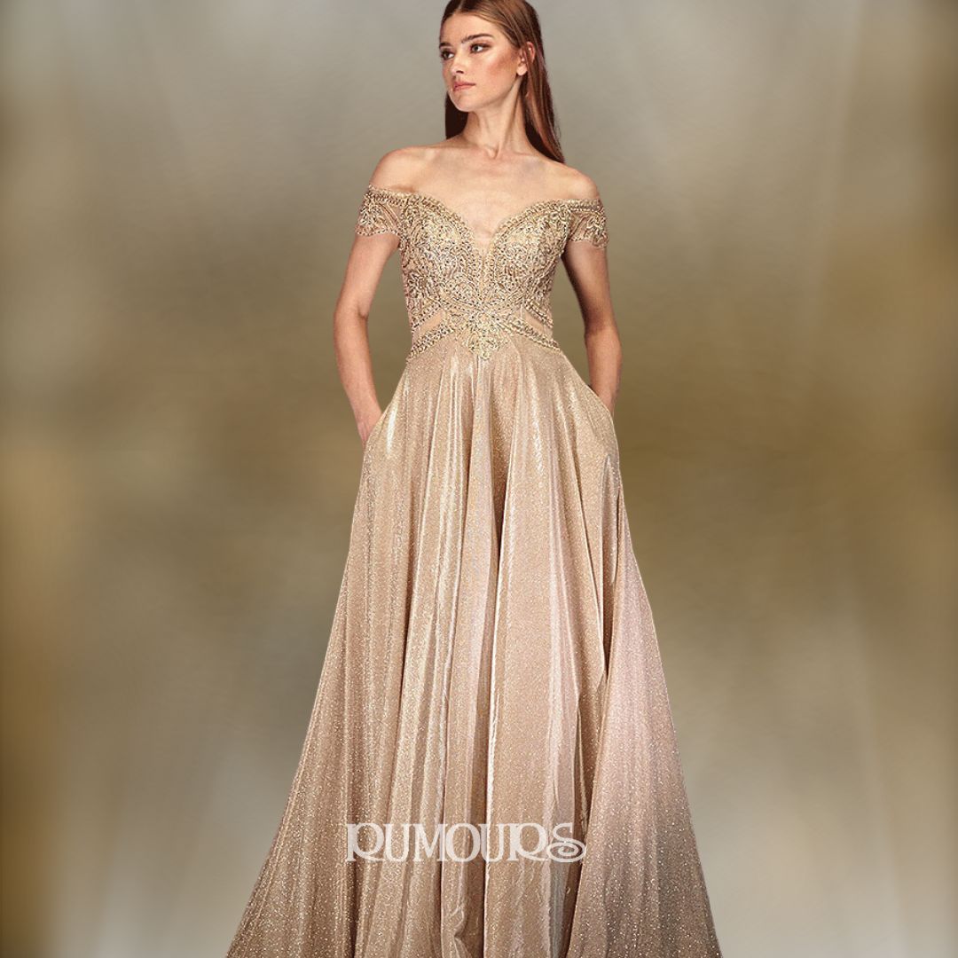 Woman in gold off-shoulder gown with embellished bodice, hands in pockets.