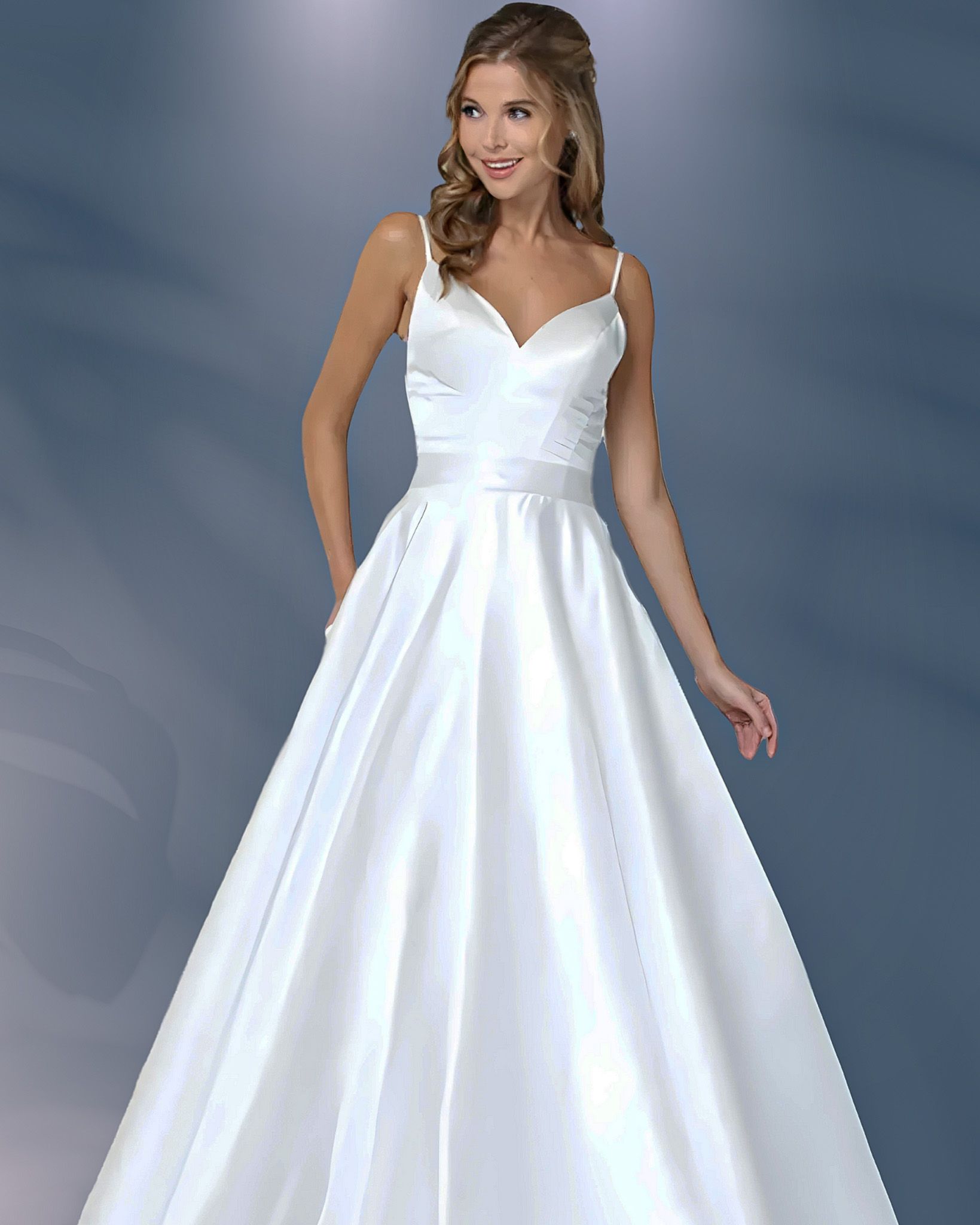 Woman in white satin wedding dress with spaghetti straps, smiling, posed in front of blue background.