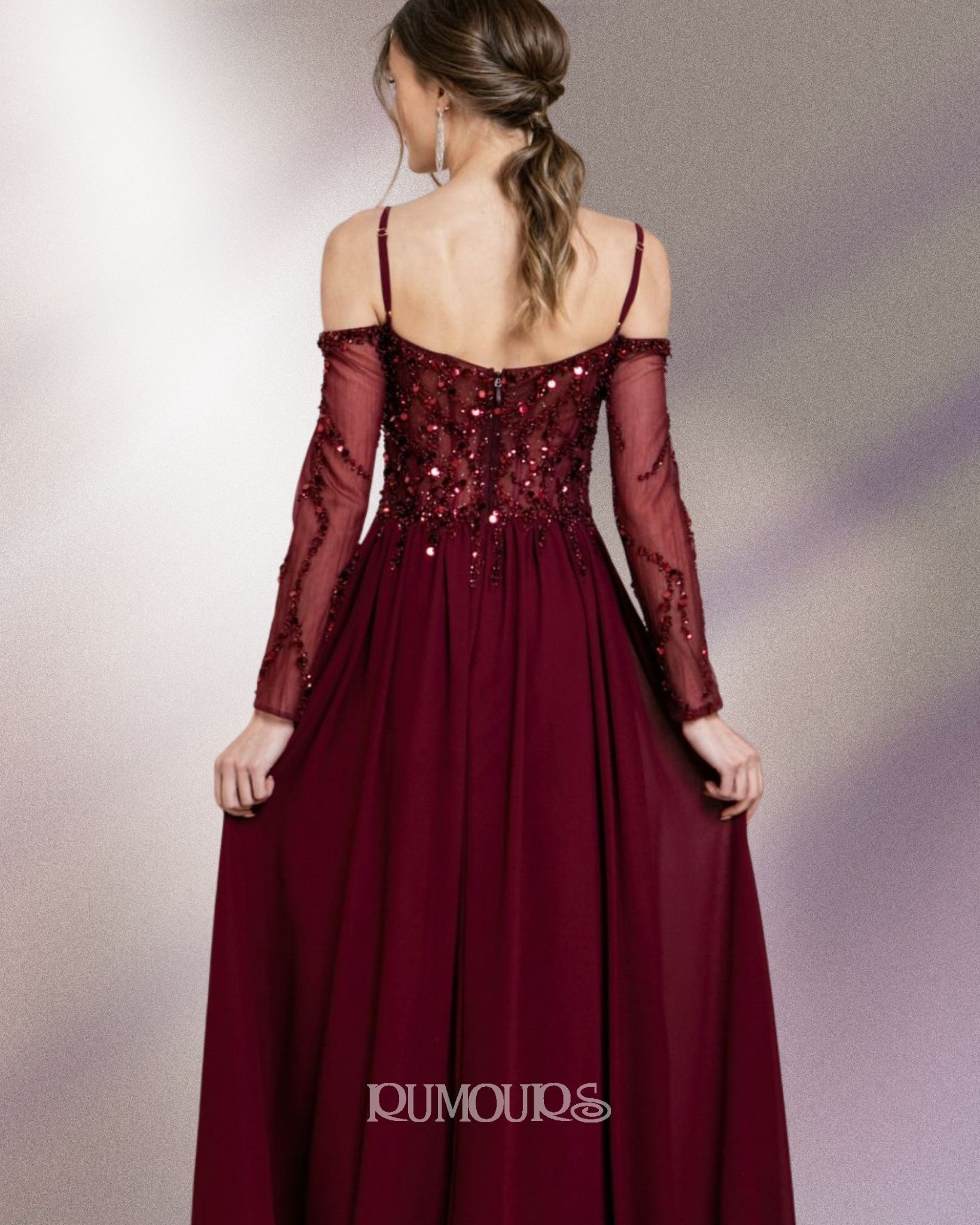 Woman in a long, dark red formal dress with off-the-shoulder sleeves, standing in front of a blurry background.