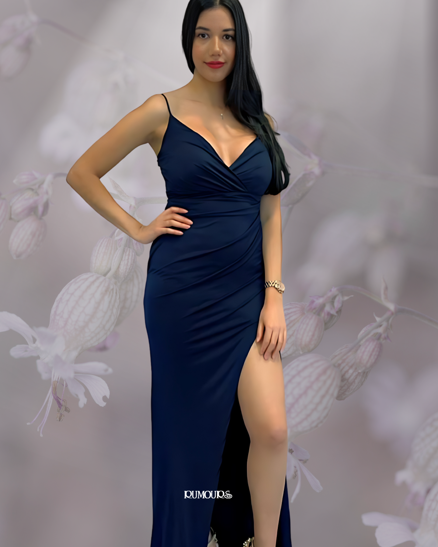 Woman in a navy blue, form-fitting dress with a high slit, posing with a hand on her hip.