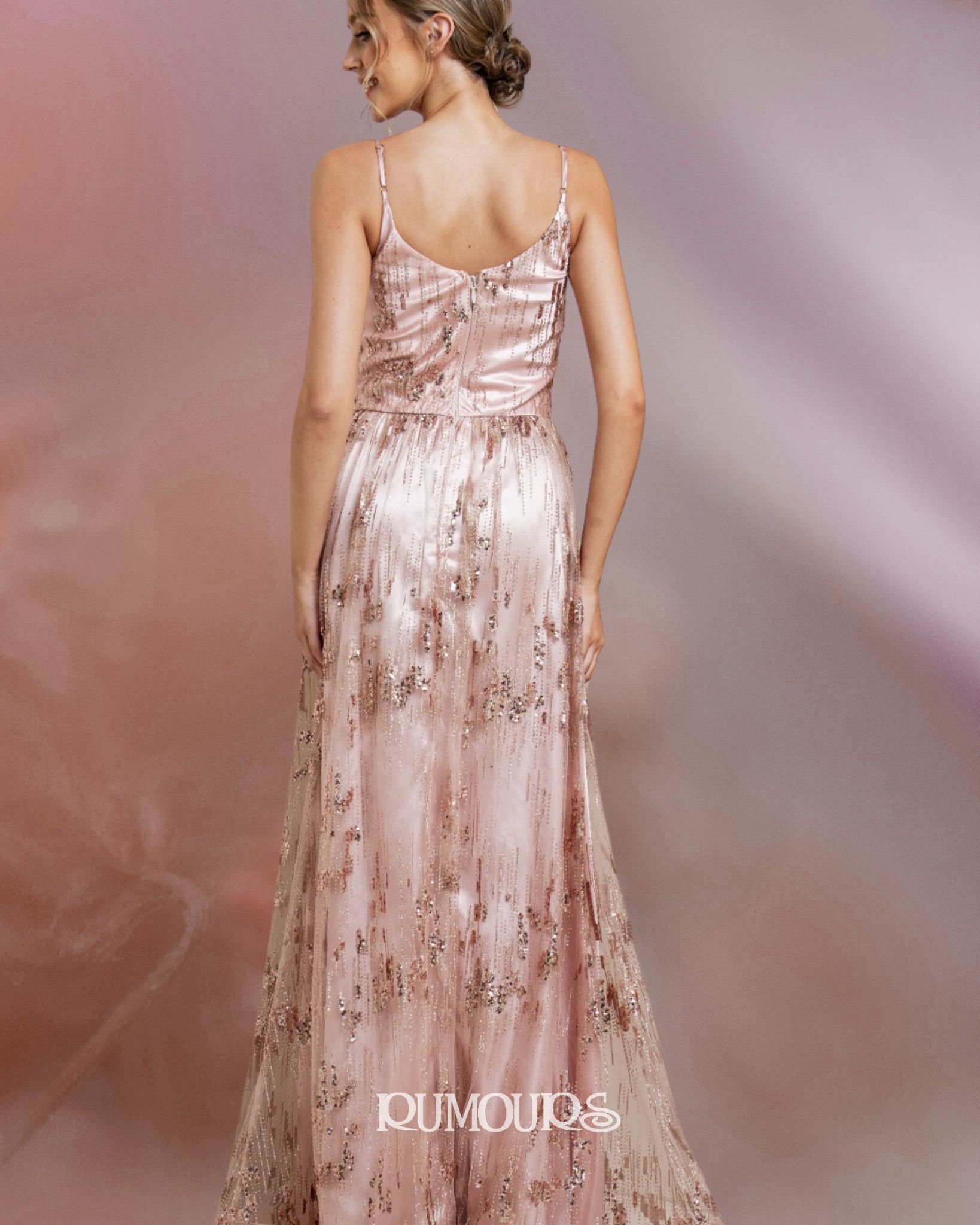 Woman in a pink, sequined formal dress, standing, looking to the side, against a pink and purple background.