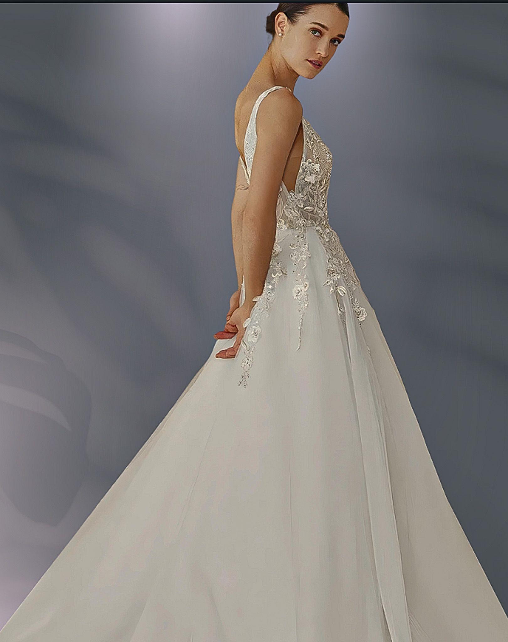 Woman in a white wedding gown, hands clasped behind her, facing the viewer. The dress has ornate bodice and a full skirt.