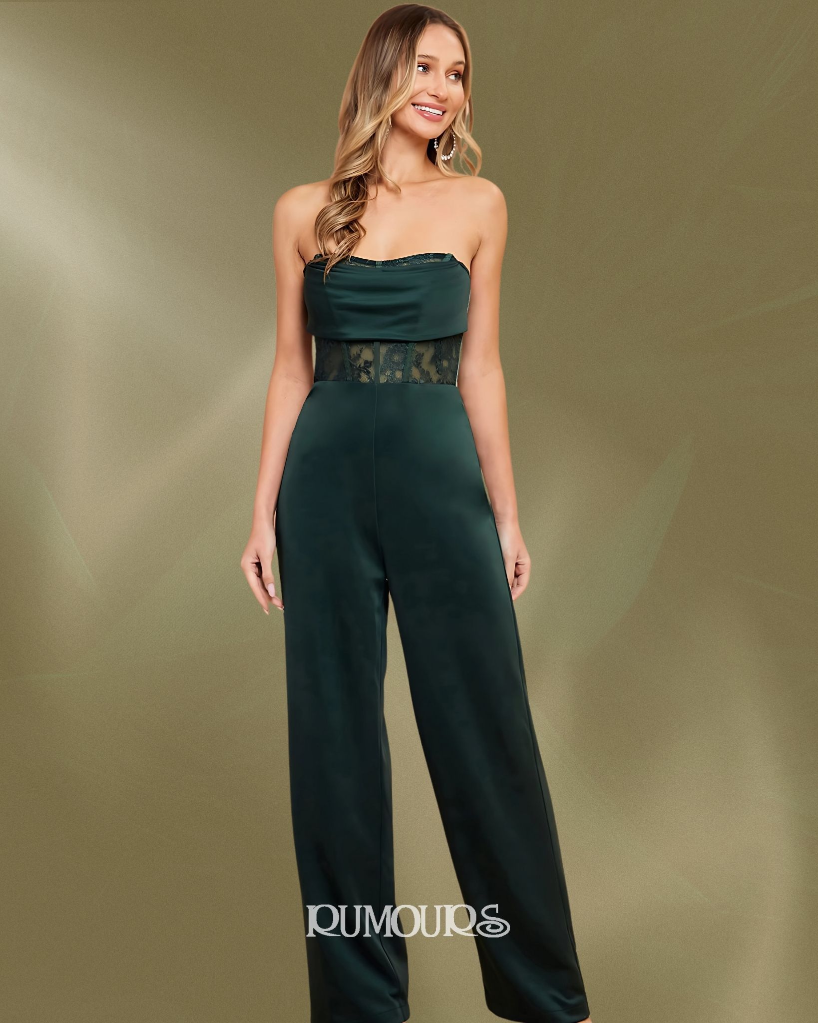 Woman in a dark green strapless jumpsuit with lace detail, standing against a neutral backdrop.