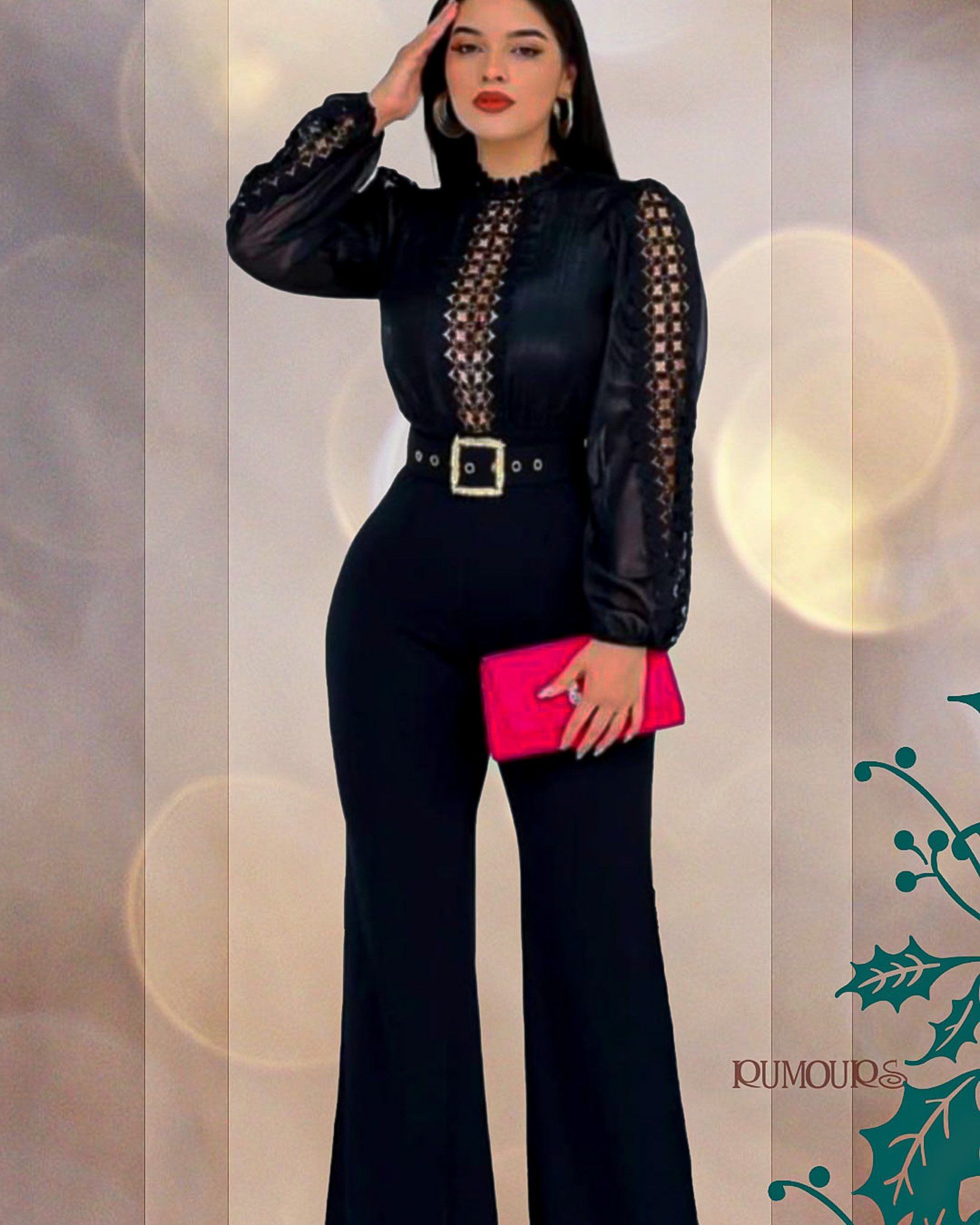 Woman in black jumpsuit with lace sleeves, holding a pink clutch, standing against a blurred background.