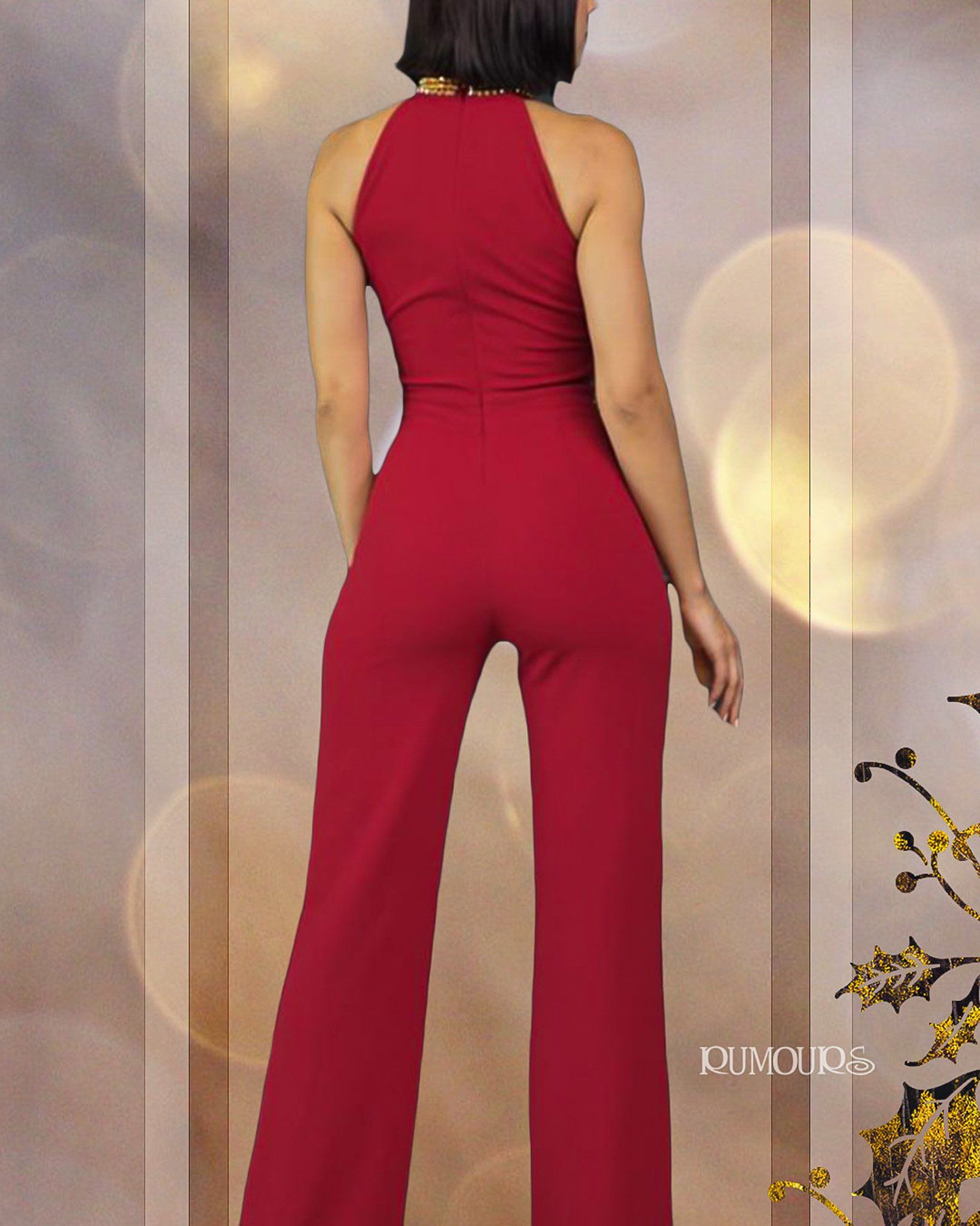 Woman in red halter jumpsuit, back view, standing in front of a neutral-toned backdrop.