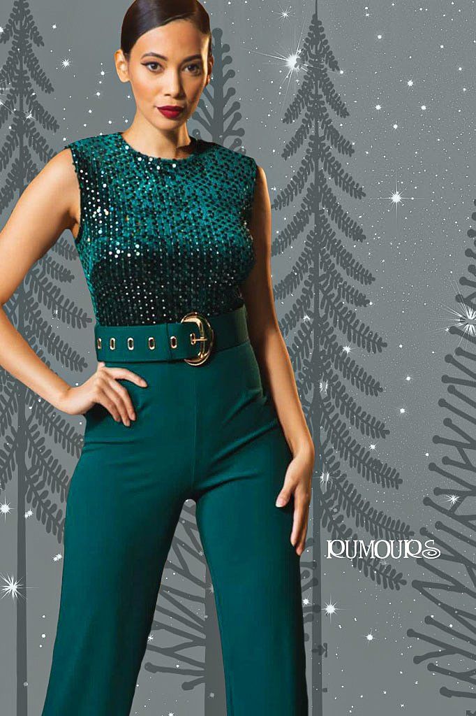 Woman in teal sequin top and pants, posing, wide belt. Gray background with trees.