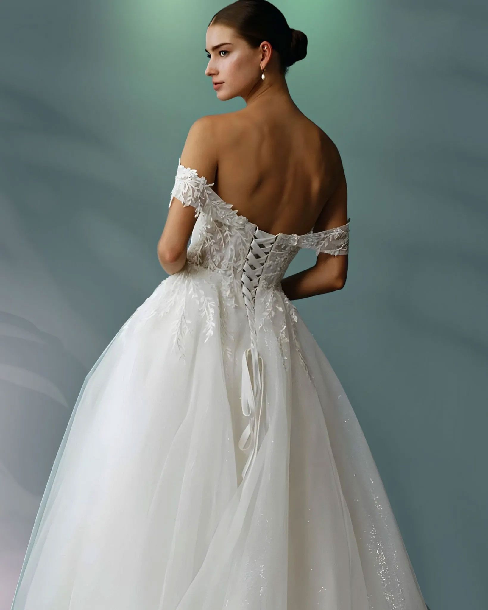 Woman in a white off-the-shoulder wedding gown, back view, with lace detailing and a full skirt.