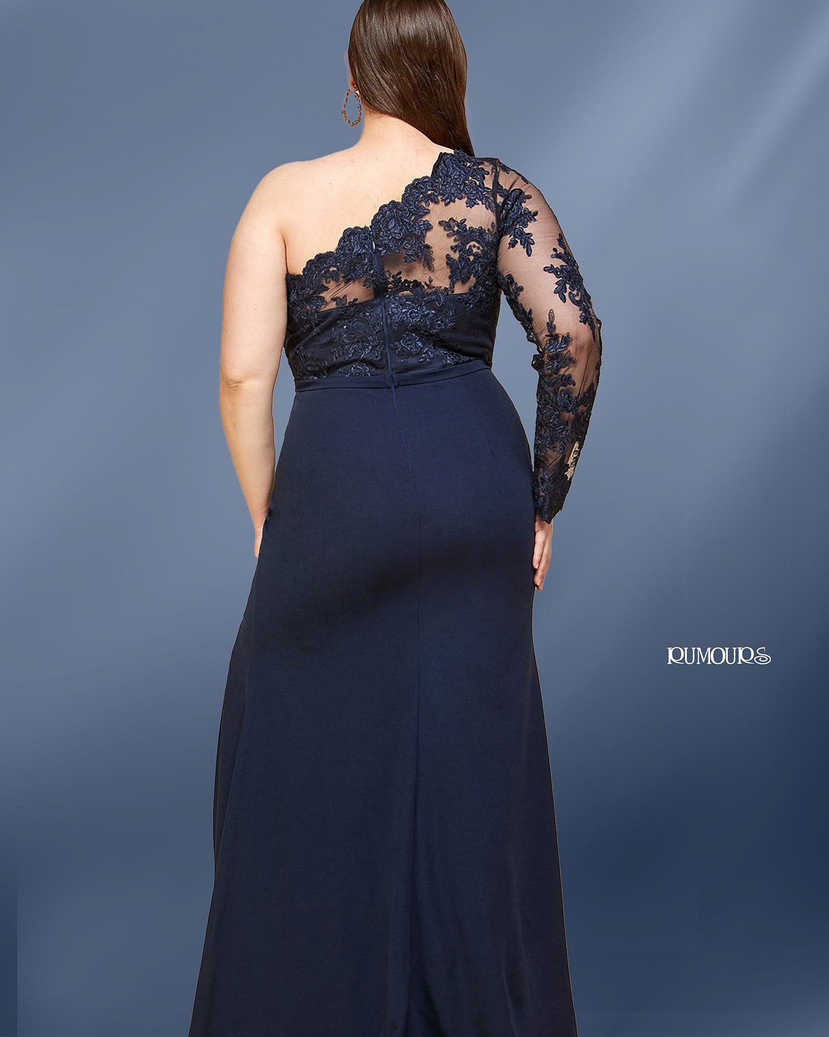 Woman in navy blue one-shoulder formal dress with floral lace sleeve, standing in front of a blue background.