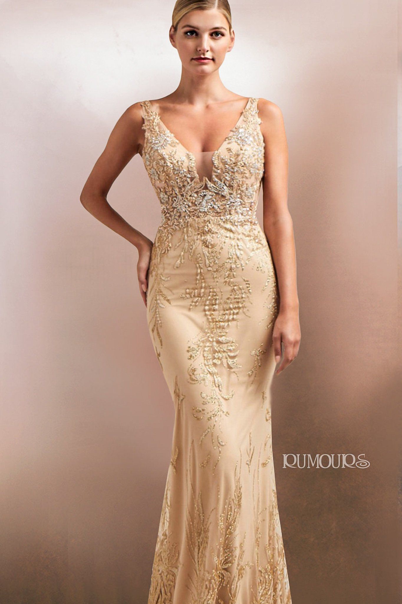 Woman in a gold formal gown, hand on hip, standing against a neutral background.