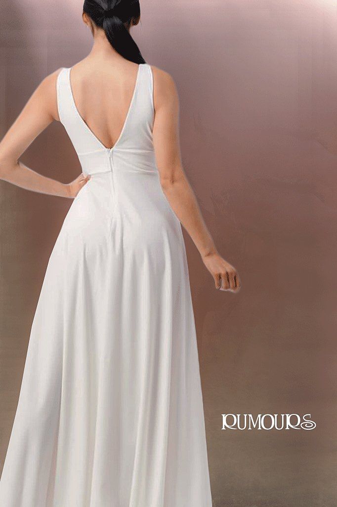 Woman in a white dress, back view, standing indoors, v-neck, flowing skirt.