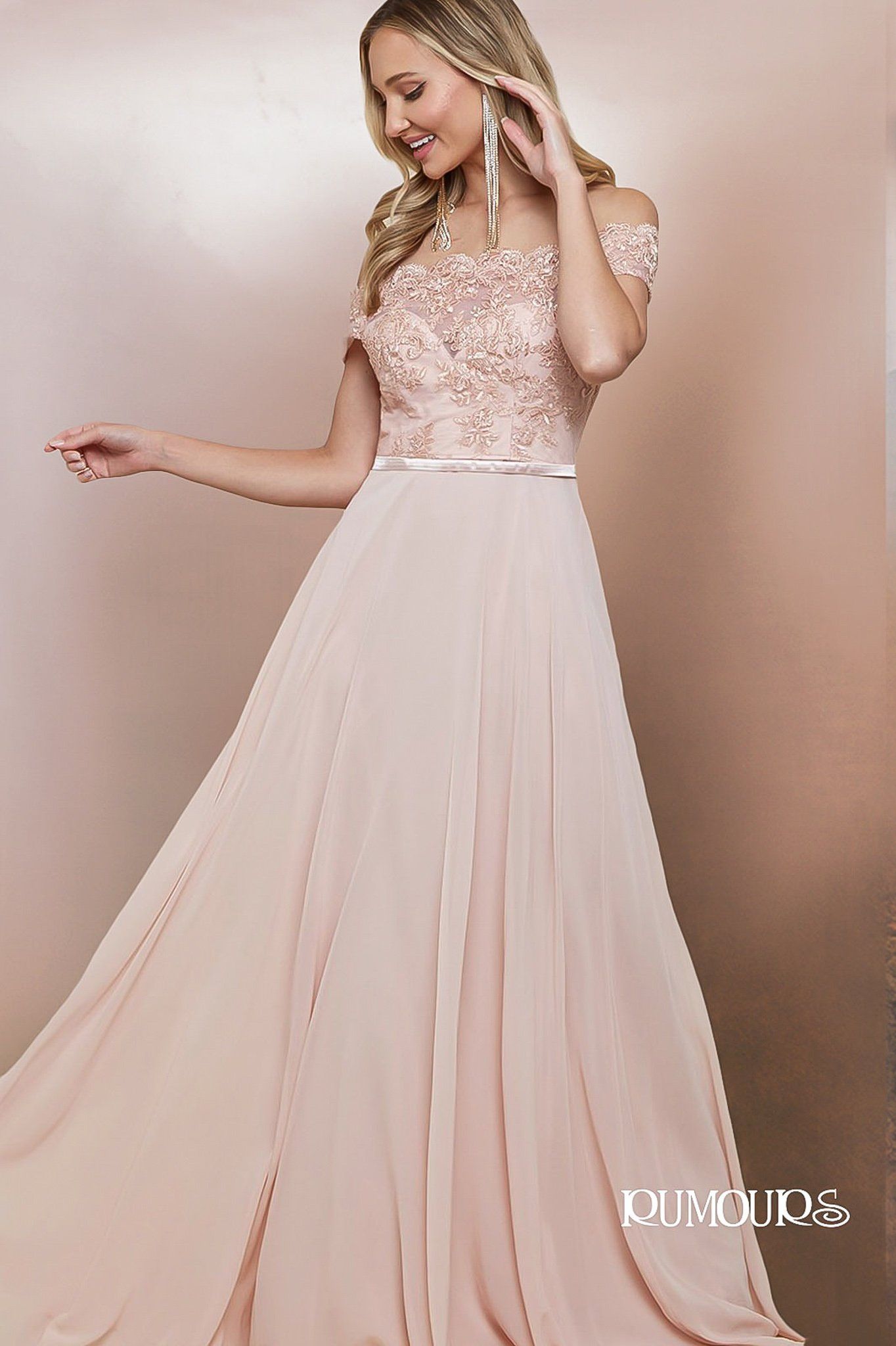 Woman in a blush-colored off-the-shoulder gown, posing with arm extended. Pink background.
