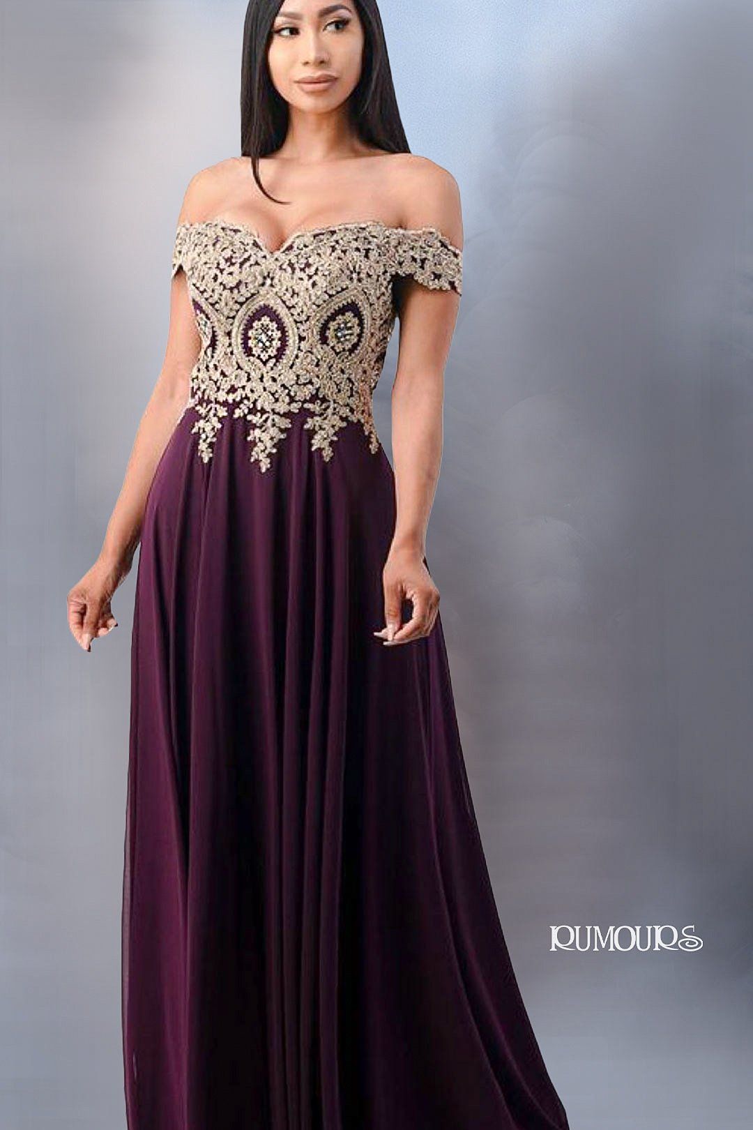 Woman in a dark purple off-shoulder gown with gold embroidered bodice, standing against a gray backdrop.