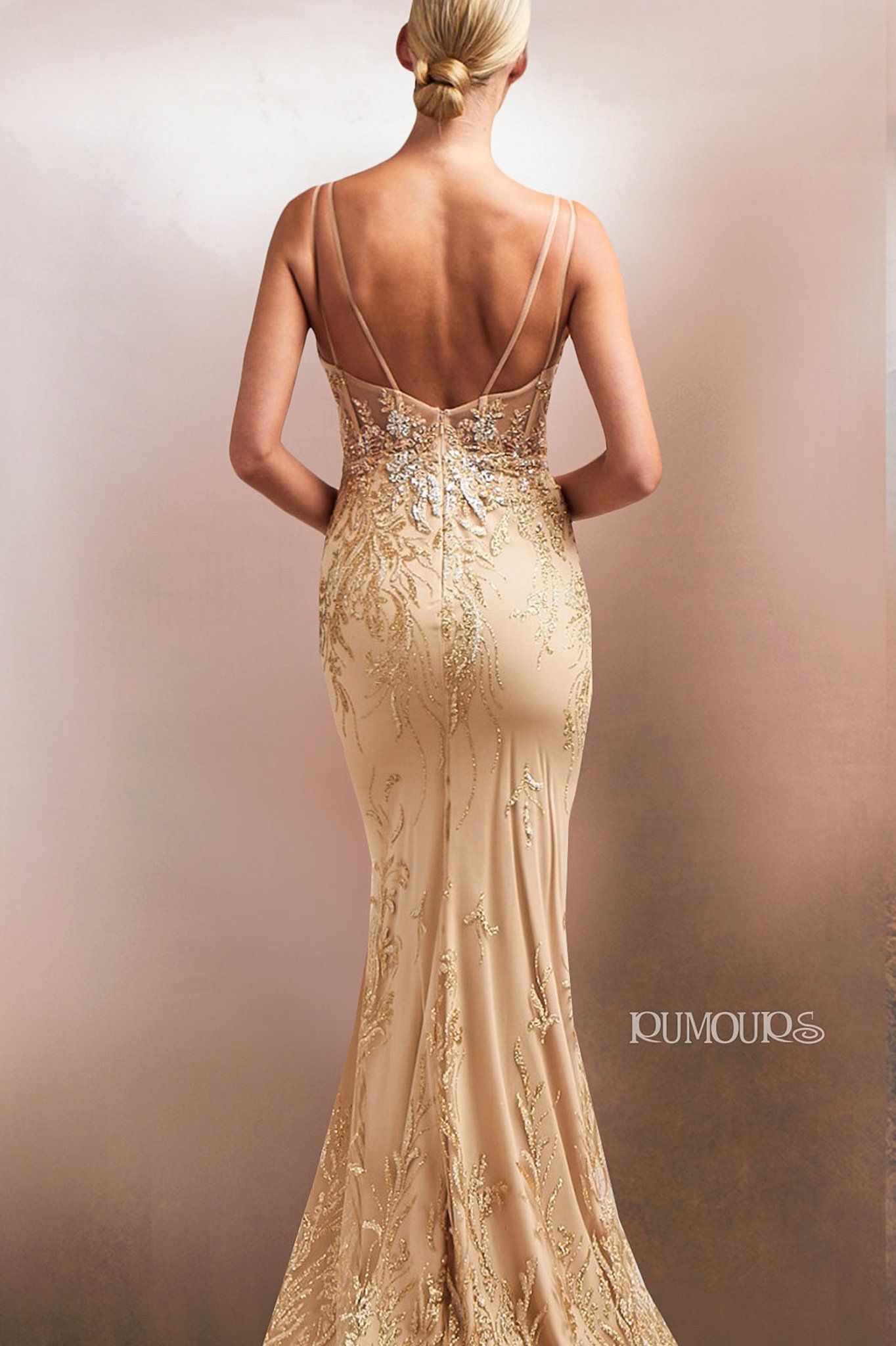 Woman in a gold evening gown with thin straps and intricate beading, back view.