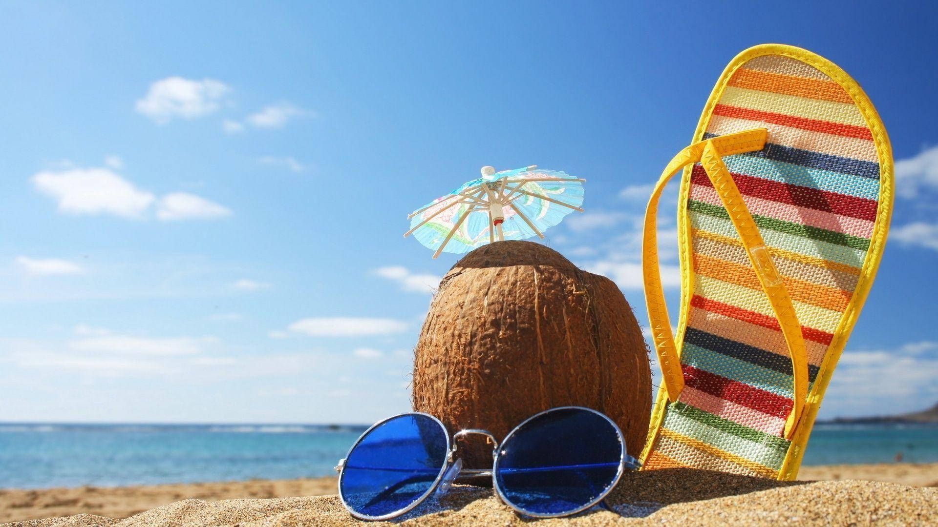 A pair of flip flops , sunglasses , and a coconut on the beach.