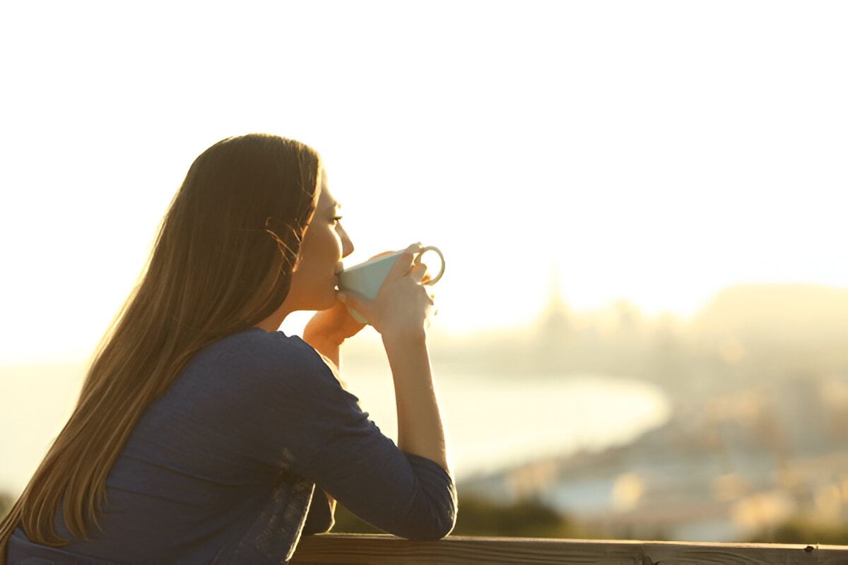 A Woman is Sitting on a Bed Drinking Coffee and Looking Out the Window  — Zen Luxury Retreats in Darwin City, NT