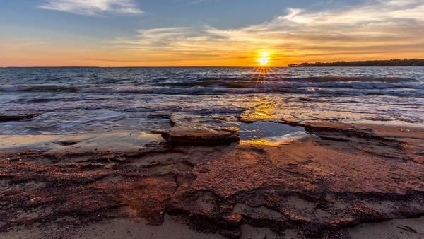 A Sunset Over a Body of Water with Rocks in The Foreground — Zen Luxury Retreats in Darwin City, NT