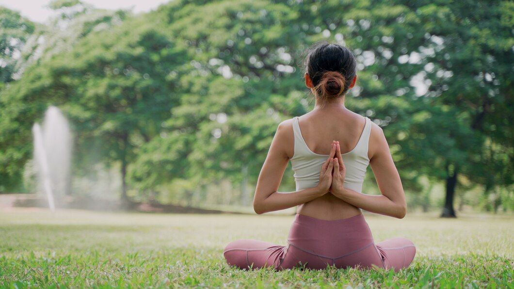 A woman is sitting in a lotus position on the grass in a park.
