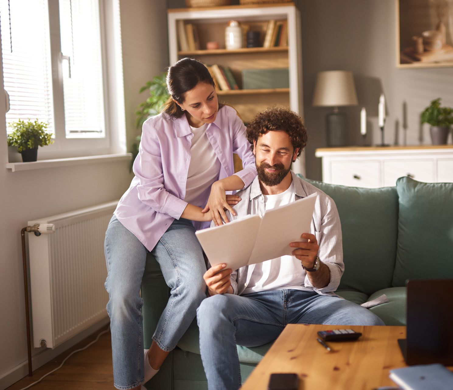 Two people review financial charts on a laptop, pointing at data; a calculator and documents are on the table.