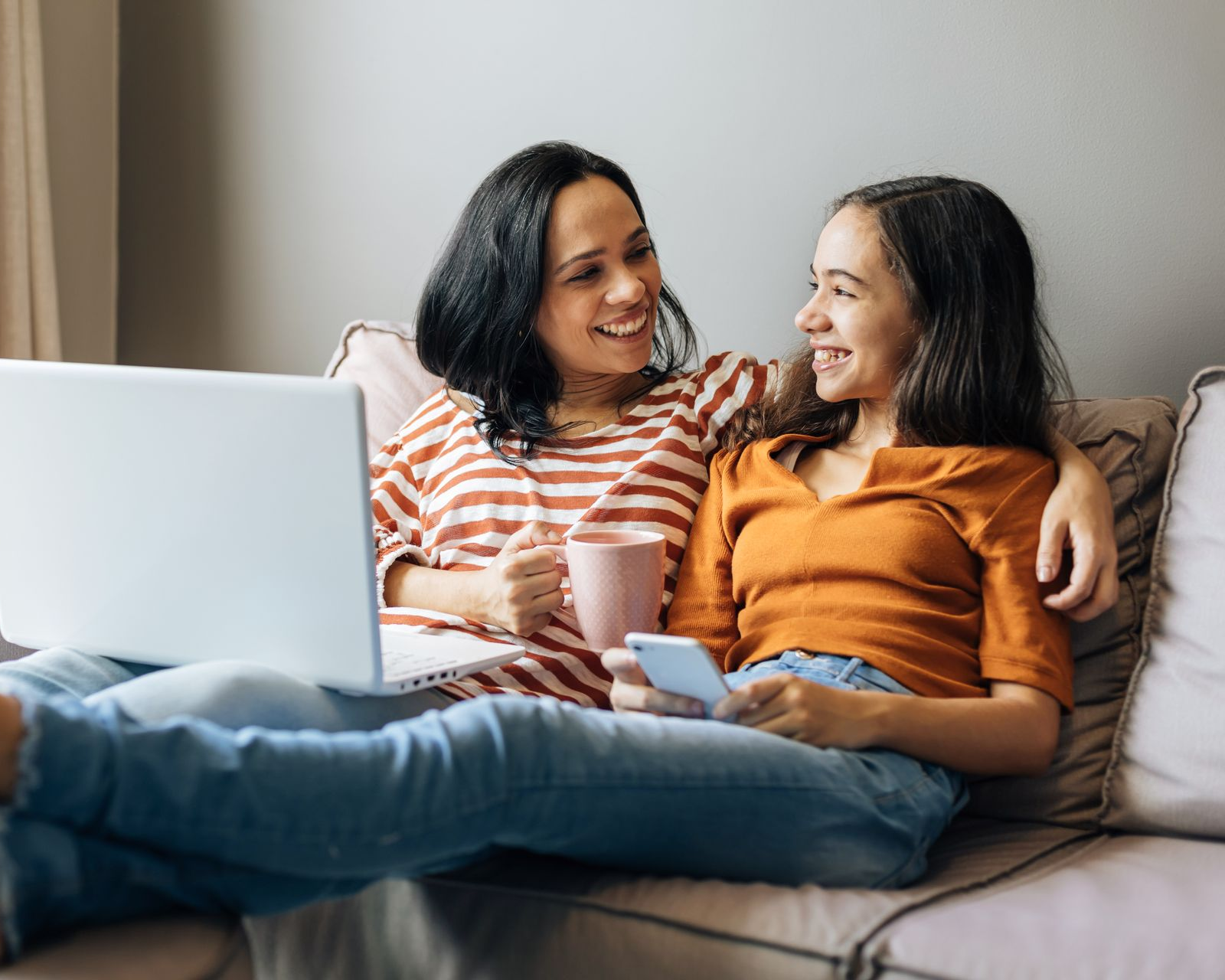 Person using a laptop with a spreadsheet on the screen, taking notes with a pen and notepad on a wooden desk.