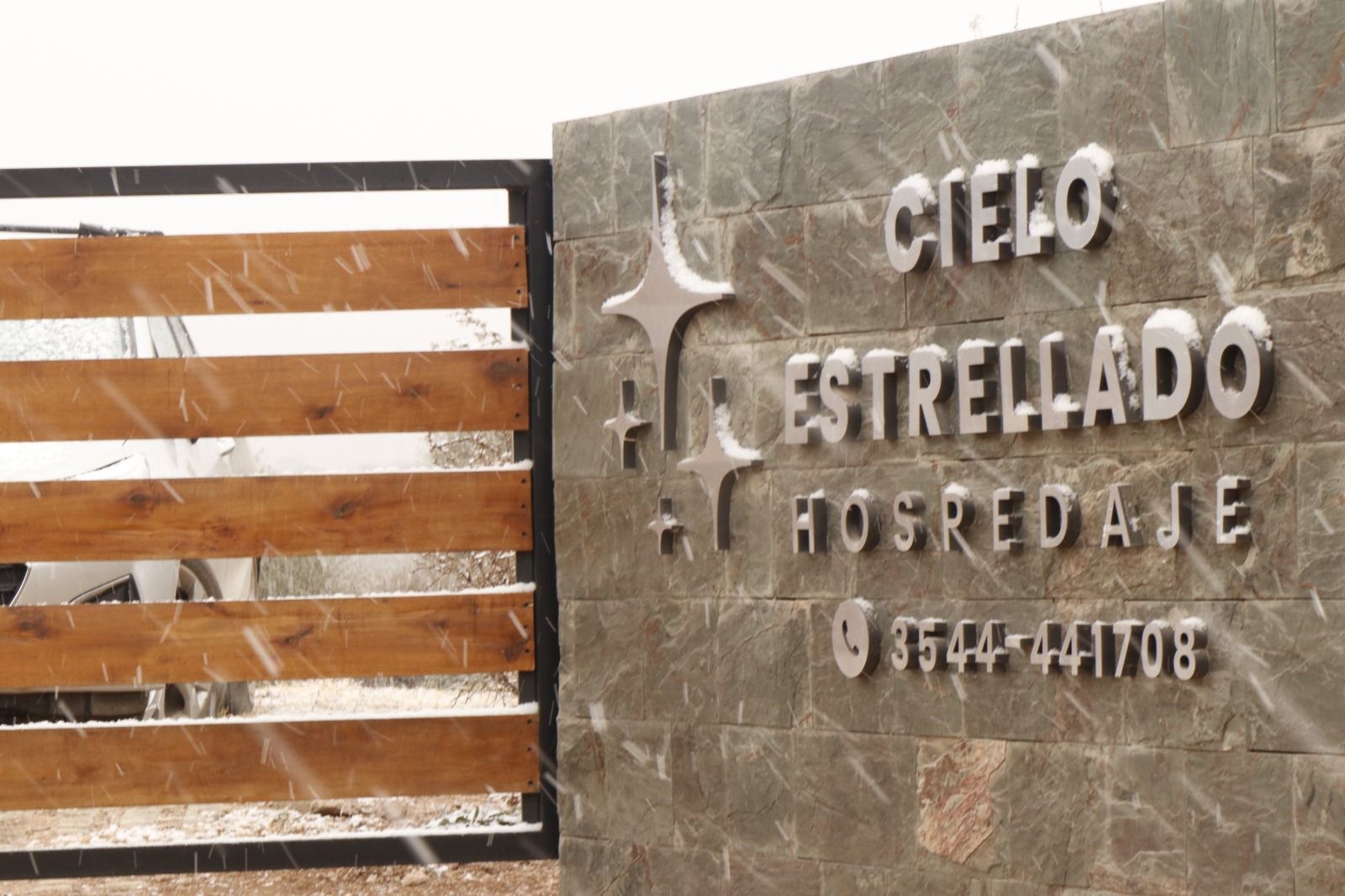 Entrance sign for Cielo Estrellado Hospedaje on a stone wall beside a wooden gate