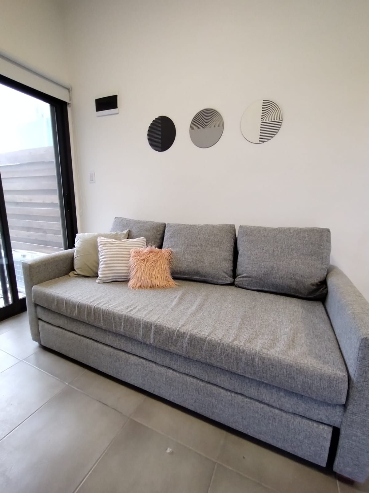 Sofá moderno gris con cojines estampados en una sala de estar minimalista cerca de una puerta corrediza de vidrio.